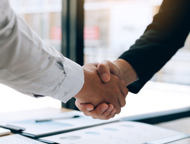Entrepreneurs collaboration deal shaking hands in a modern office and financial paper graph on desk.