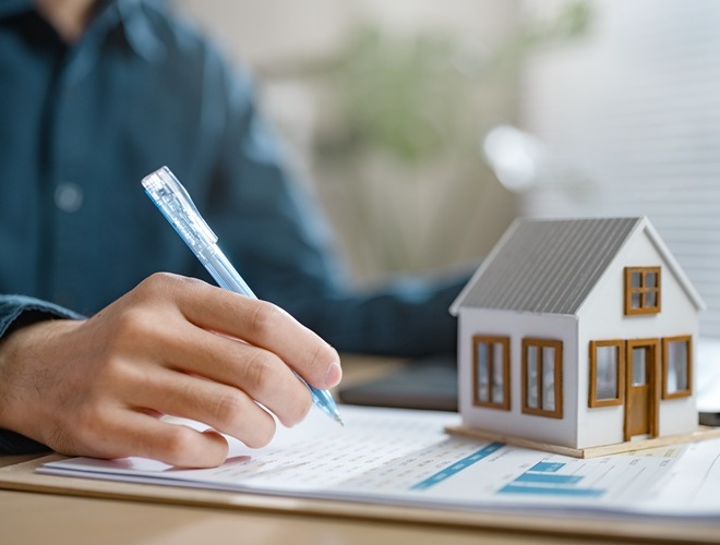 estate, property, residential, investment, calculator, domestic, construction, insurance, mortgage, agreement. A man is writing on a piece of paper with a pen. The man is focused on his writing.