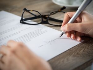 Closeup shot of a woman signing a form. She's writing on a financial contract. Shallow depth of field with focus on tip of the pen.
